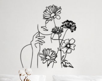 Puede incluir: Arte de pared de metal negro con un dibujo de línea de la cara de una mujer con flores. Las flores son estilizadas y tienen un aspecto delicado y femenino.
