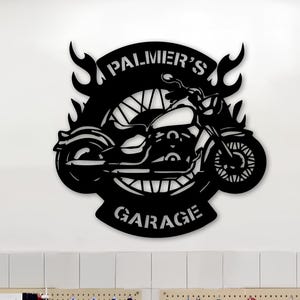 Peut inclure: Panneau de moto en métal noir avec le texte "Palmer's Garage" et des flammes. Le panneau est monté sur un mur blanc au-dessus d'un atelier de garage avec des outils et des pneus.