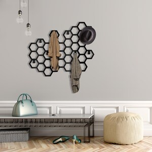 May include: Black metal hexagonal wall mounted coat rack with hooks. A brown jacket, a patterned scarf, a black hat, and a silver handbag are hanging on the hooks.