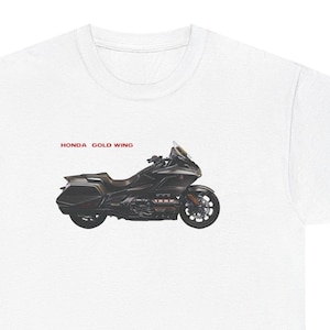 May include: A white short-sleeve t-shirt featuring a graphic of a black Honda Gold Wing motorcycle centered on the chest. The text HONDA GOLD WING is printed in red above the motorcycle graphic. The shirt has a crew neckline and short sleeves.