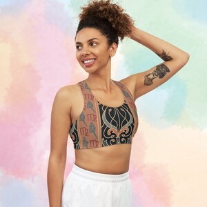 May include: A black, brown, and blue sports bra with a repeating pattern of the astrological sign Virgo. The bra has a racerback style and is made of a stretchy, breathable fabric.