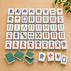 May include: A collection of white rectangular mahjong tiles with green backs, featuring various engraved characters, numbers, and symbols in red, blue, and green ink, arranged in a grid pattern with several loose tiles placed in the foreground.