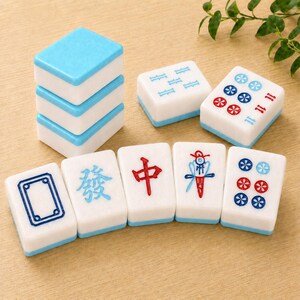 May include: A set of white mahjong tiles with light blue backs. The tiles feature various engraved symbols in blue and red, including Chinese characters, floral patterns, and geometric shapes. Some tiles are stacked in a column of three.