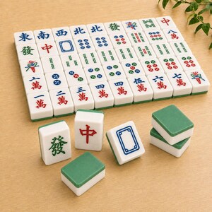 May include: A set of white and green Mahjong tiles featuring various engraved characters, symbols, and numbers in red, blue, and green ink. The tiles are arranged in a grid pattern with several individual tiles placed in the foreground.