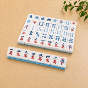 May include: A set of white rectangular Mahjong tiles arranged in a grid and a single row. The tiles feature blue and red Chinese characters, numerical symbols, and decorative icons. Each tile has a smooth surface and a light blue base edge.