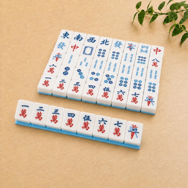 May include: A set of white rectangular Mahjong tiles arranged in a grid and a single row. The tiles feature blue and red Chinese characters, numerical symbols, and decorative icons. Each tile has a smooth surface and a light blue base edge.
