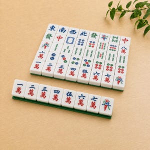 May include: A set of white rectangular Mahjong tiles featuring various colorful Chinese characters, numbers, and symbols in red, blue, and green ink. The tiles are arranged in a grid formation with a single row placed on a green rack in front.