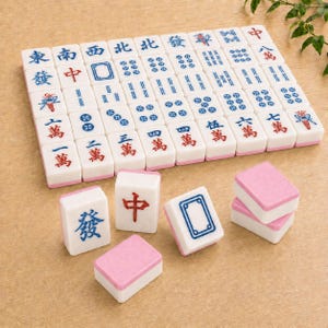 May include: A set of white Mahjong tiles with pink backs, featuring various blue and red Chinese characters, symbols, and numerical patterns. The tiles are arranged in a grid formation with several individual tiles placed in the foreground.