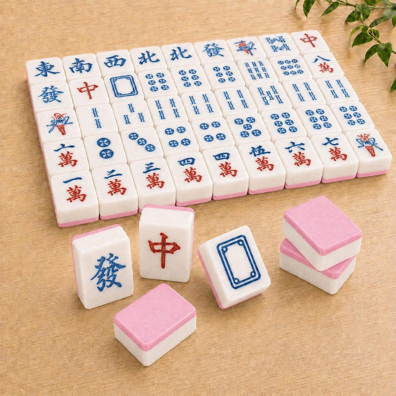 May include: A set of white Mahjong tiles with pink backs, featuring various blue and red Chinese characters, symbols, and numerical patterns. The tiles are arranged in a grid formation with several individual tiles placed in the foreground.