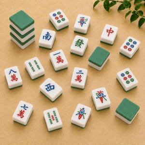 May include: A collection of rectangular Mahjong tiles featuring white faces with various colorful Chinese characters, bamboo patterns, and circular designs, alongside solid green-backed tiles, some stacked and others scattered.