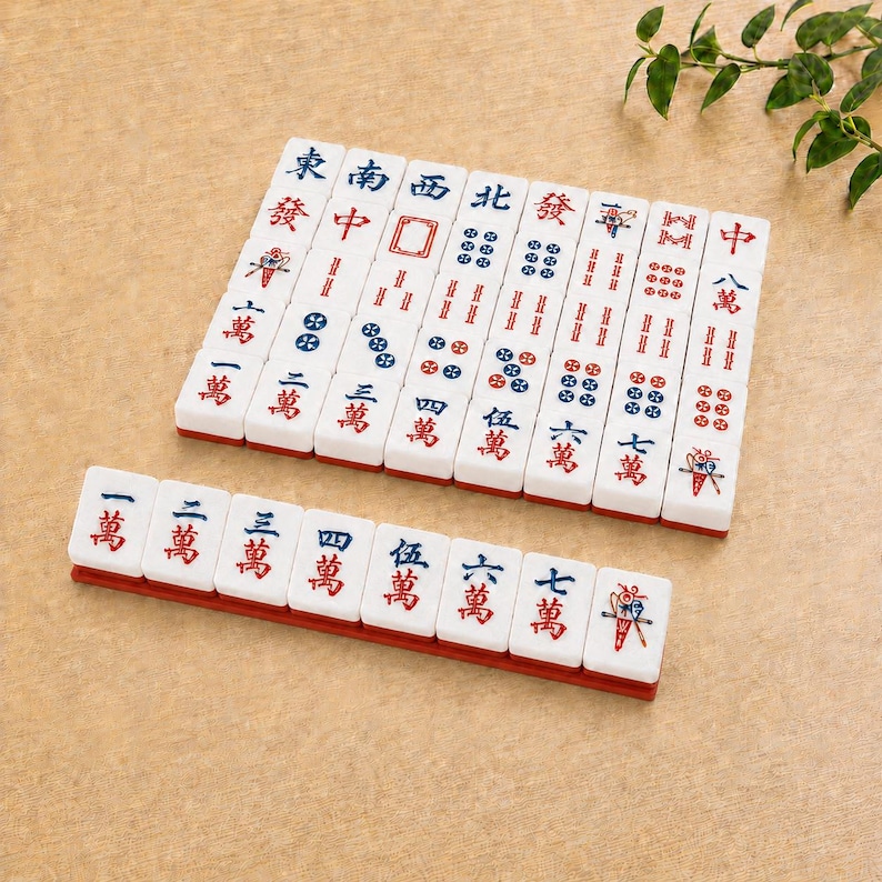 May include: A set of white rectangular Mahjong tiles featuring red and blue engraved Chinese characters and symbols. The tiles are arranged in a neat grid and a single horizontal row, displaying various numerical values and directional markers.