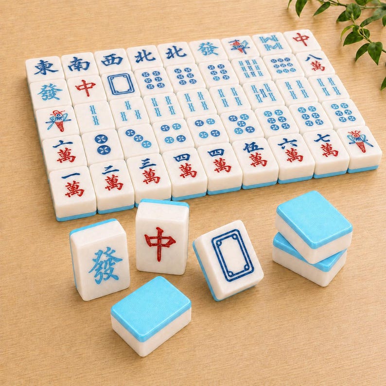 May include: A set of white rectangular mahjong tiles with blue and red engraved characters and symbols. The tiles feature various Chinese characters, dots, and bamboo patterns, with some tiles displayed upright and others showing blue backs.