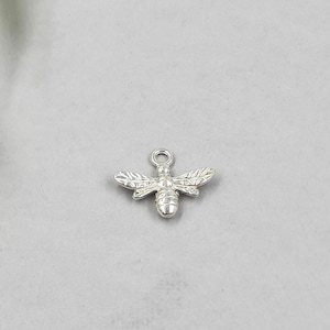 May include: Silver bee charm with detailed wings and a textured body. The charm has a loop at the top for attaching to jewelry.