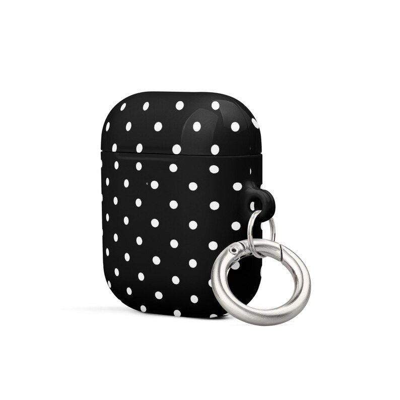 May include: Black silicone case with white polka dots for AirPods with a silver carabiner clip.