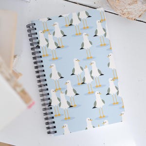 May include: A blue spiral notebook with a white and yellow seagull pattern. The notebook has a white background with a repeating pattern of seagulls.
