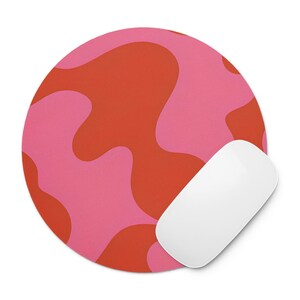 May include: A round mousepad with a pink and orange abstract pattern. A white wireless mouse is positioned on the right side of the mousepad. The mousepad has a smooth surface and is designed for computer use.