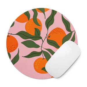 May include: Round mousepad with a pink background featuring a pattern of orange oranges, green leaves, and stems. A white computer mouse is positioned on the right side of the mousepad. The mousepad is designed for computer use.