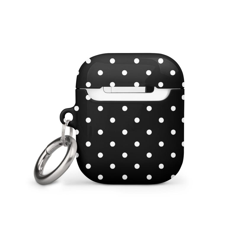 May include: Black and white polka dot silicone case with a silver keychain for Apple AirPods.
