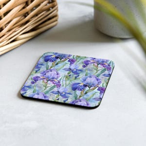 May include: A square coaster featuring a watercolour design of purple iris flowers on a light blue background.