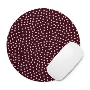 May include: Round mousepad with a burgundy background and a pattern of small, evenly spaced pink polka dots. A white computer mouse is positioned on the right side of the mousepad.