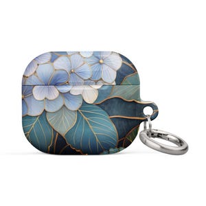 Op de afbeelding: Een AirPod-hoesje met bloemenpatroon, met blauwe en witte bloemen met gouden accenten op een teal achtergrond. Het heeft een zilverkleurige metalen ring voor bevestiging.