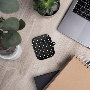 May include: A black and white polka dot Airpods case with a white strap.