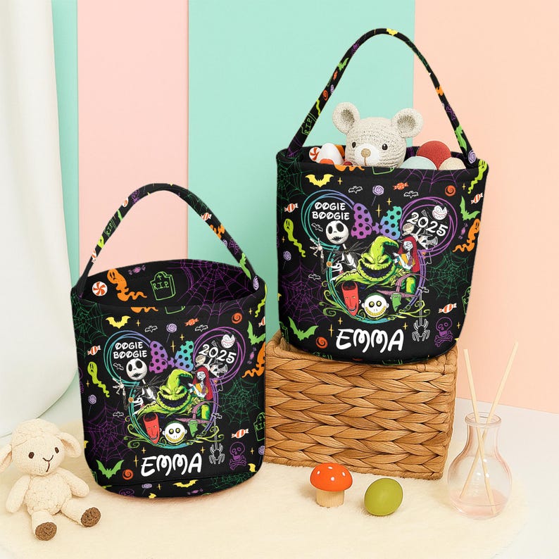 May include: Two black Halloween-themed tote bags with handles, featuring a Nightmare Before Christmas design. The bags have a circular design with the words "Oogie Boogie" and "2025" and the name "Emma". One bag contains a stuffed animal and colorful balls.
