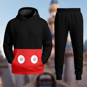 A black hoodie with a red pocket and a pair of black sweatpants are shown against a blurred background.