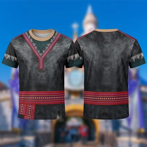 May include: A black t-shirt with a design inspired by a character from the movie Frozen. The shirt features a V-neck with red and green accents, a red band at the waist, and short sleeves. The background is blurred.
