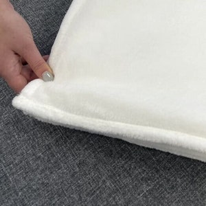 May include: A white plush throw blanket with a soft, fuzzy texture. The blanket is folded and has a subtle seam around the edge.
