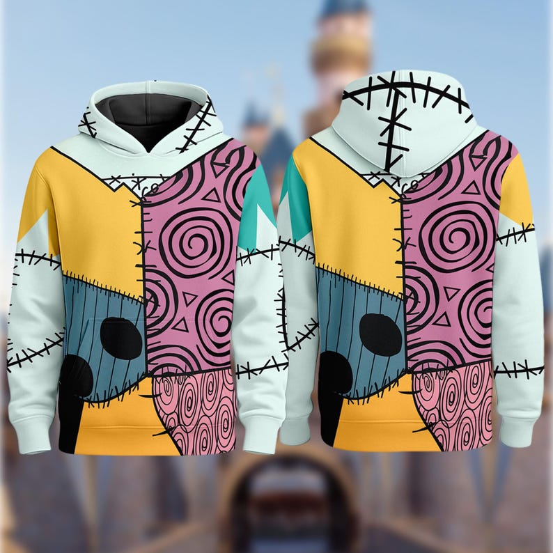 May include: A light blue hoodie with a patchwork design featuring yellow, pink, and blue panels. The design includes black stitching and spiral patterns, resembling a character from a movie. The hoodie has a white hood and cuffs.