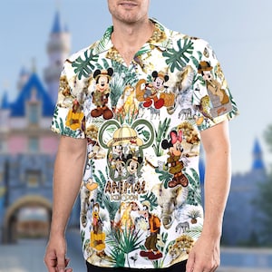 May include: White button-down shirt with a tropical print featuring Mickey Mouse and friends in safari outfits. The print includes zebras, lions, and other jungle animals. The shirt has a collar and short sleeves. The text "Animal Kingdom" is printed on the shirt.