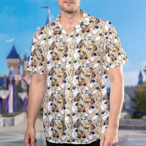 May include: A tan short-sleeved button-down shirt with a repeating pattern of white robots. The robots are in various poses and have black eyes and mouths.