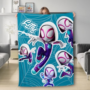 May include: A blue and white fleece blanket with a spiderweb design and multiple images of Spider-Gwen, a superhero character. The text "Lilly" is printed on the blanket.