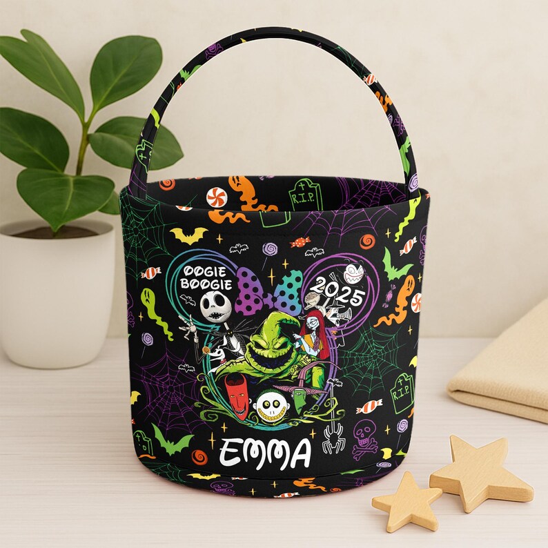 May include: Black Halloween bucket with a colorful design featuring characters and text from "The Nightmare Before Christmas." The bucket has a handle and the name "Emma" printed on the front. The design includes the text "Oogie Boogie" and "2025."