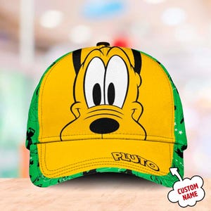 May include: A yellow and green baseball cap with a cartoon image of Pluto's face on the front. The cap has the word "PLUTO" written in yellow on the brim. The cap has a green and black pattern on the sides.