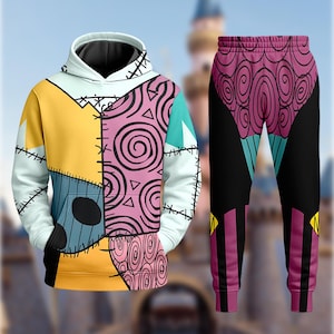 May include: A matching hoodie and sweatpants set. The hoodie features a patchwork design in yellow, blue, pink, and white, with black stitching details. The sweatpants are black with a pink and purple swirl pattern on the upper portion.