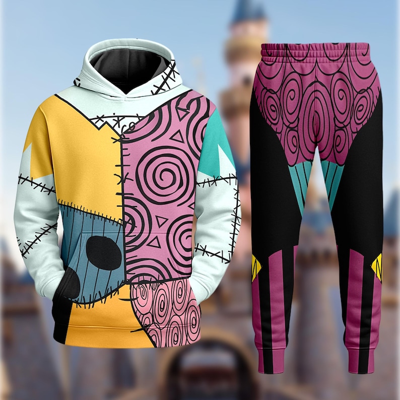 May include: A matching hoodie and sweatpants set. The hoodie features a patchwork design in yellow, blue, pink, and white, with black stitching details. The sweatpants are black with a pink and purple swirl pattern on the upper portion.