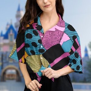 May include: A short-sleeved button-up shirt with a patchwork design featuring various colors and patterns, including black, pink, blue, yellow, and white. The shirt has a collar and a button closure.