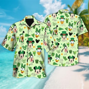 May include: Two short-sleeved button-down shirts with a light green background. The shirts are covered in cartoon character faces, shamrocks, and other St. Patrick's Day themed graphics. The characters include Mickey Mouse, Minnie Mouse, Donald Duck, and Pluto.