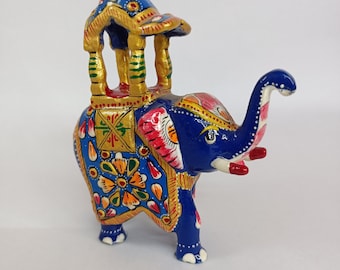 May include: A vibrantly painted wooden elephant figurine in shades of blue, gold, red, and pink. The elephant has a decorative carriage on its back. The figurine is a detailed piece of folk art.
