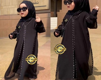 May include: Two young girls wearing black abayas with rhinestones and matching black hijabs. Both girls are wearing sunglasses. The abayas have a sheer overlay. The image has a "Best Seller" badge.