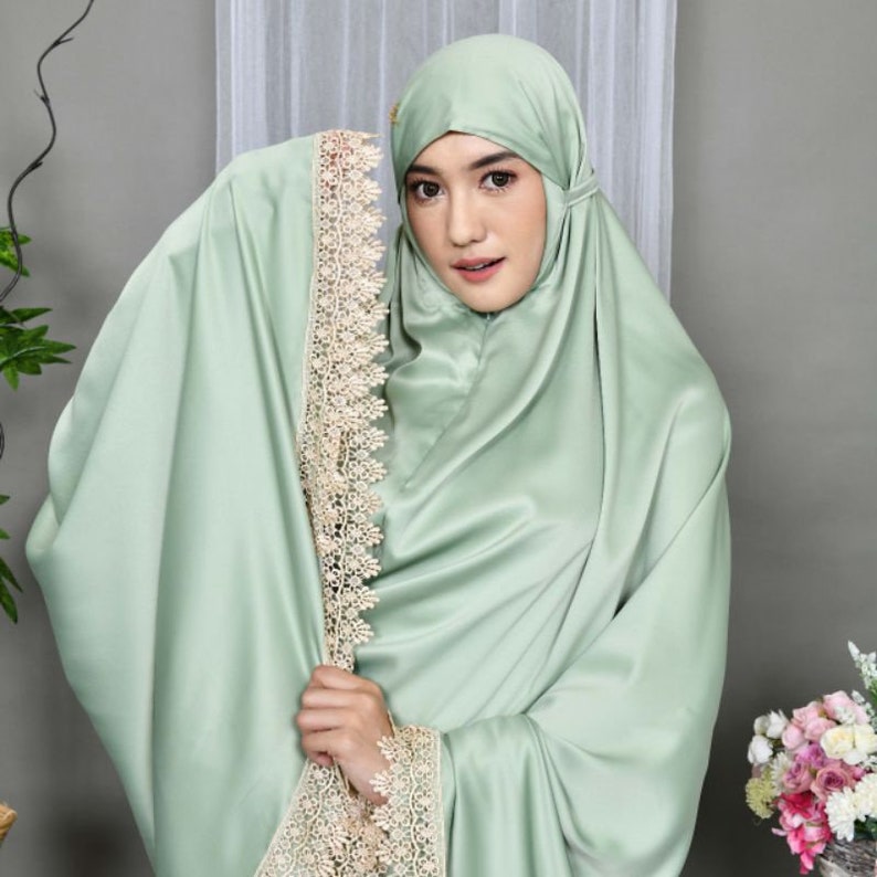 May include: A light green prayer shawl with delicate lace trim. The shawl is made of a soft, silky fabric and has a flowing drape.