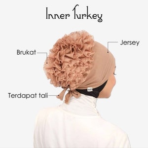 May include: A brown jersey inner cap with a large brown lace flower on top. The cap has a tie at the back and the words "Inner Turkey" are written above the cap.