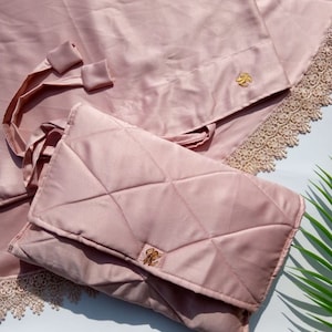 May include: A pink quilted prayer rug with a matching pink carrying case. Both items feature a gold-colored emblem.