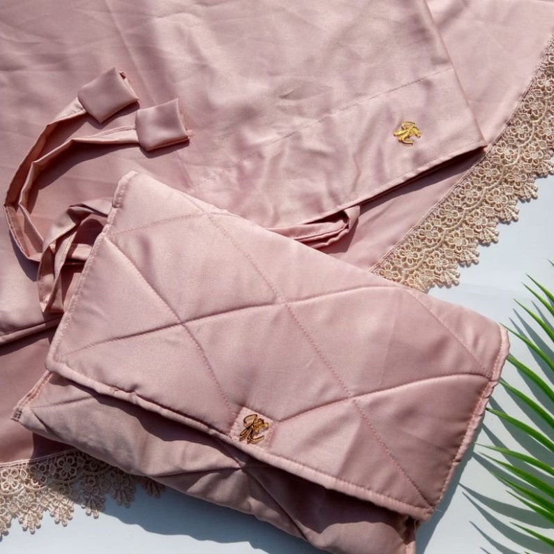 May include: A pink quilted prayer rug with a matching pink carrying case. Both items feature a gold-colored emblem.