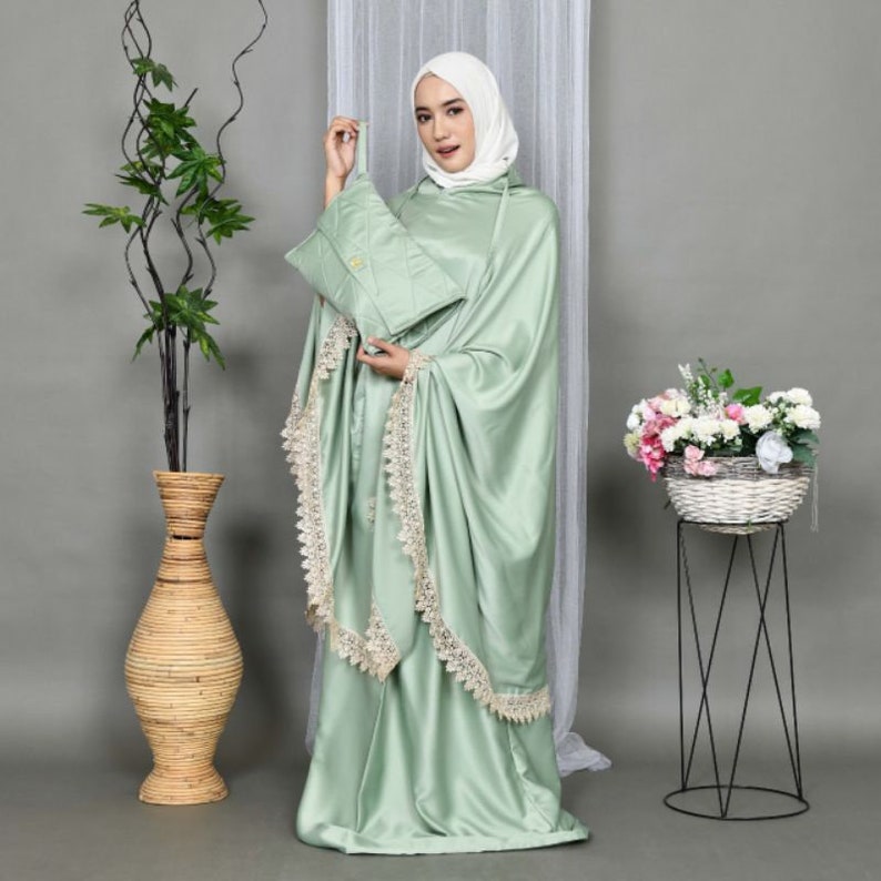 May include: A light green prayer shawl with lace trim and a matching prayer rug. The shawl has a hood and is made of a soft, silky fabric.