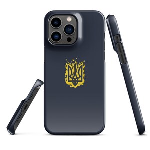 Może przedstawiać: Etui na telefon w kolorze granatowym z złotym symbolem trójzębu w płomieniach. Etui jest zaprojektowane do telefonu iPhone z wystającym aparatem.
