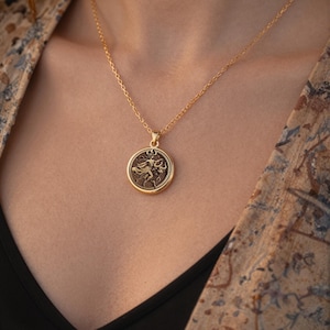 taurus woman zodiac gold pendant necklace, polished outer rim, antiqued/darkened interior field with raised relief details, circular pendant with a raised figure (appearing to be a standing human-like form) surrounded by crescent shapes and decora...
