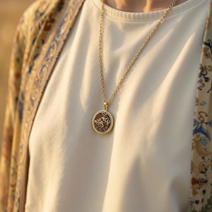 taurus woman zodiac gold pendant necklace, polished with high reflectivity on rim and bail; central field shows darker, non-reflective finish, circular pendant with raised relief figure in flowing garment, surrounded by concentric decorative borde...